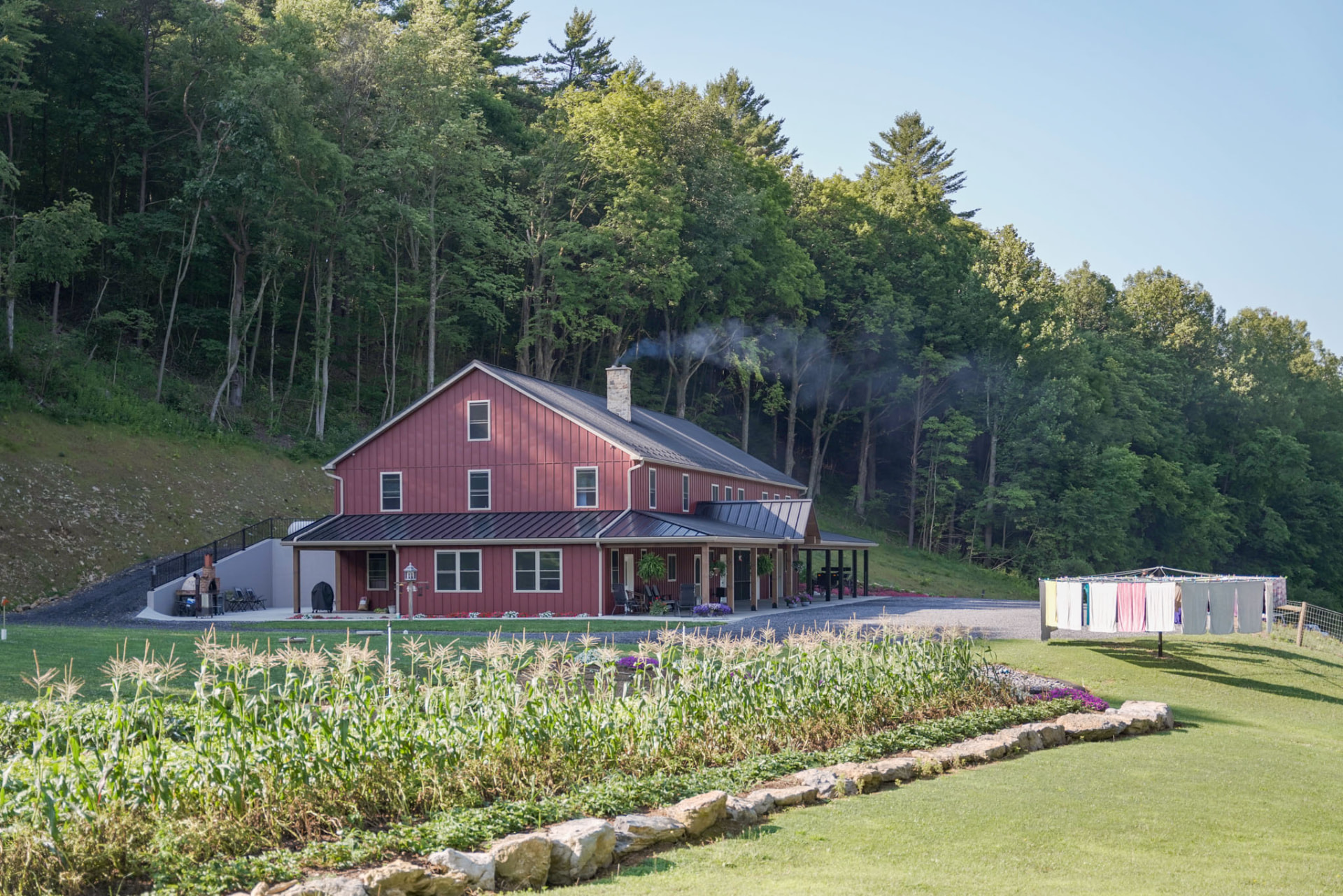 Peachy Residence — side view of a red barndominium with metal roof and covered porch above a garden — KB Builders, McVeytown, PA
