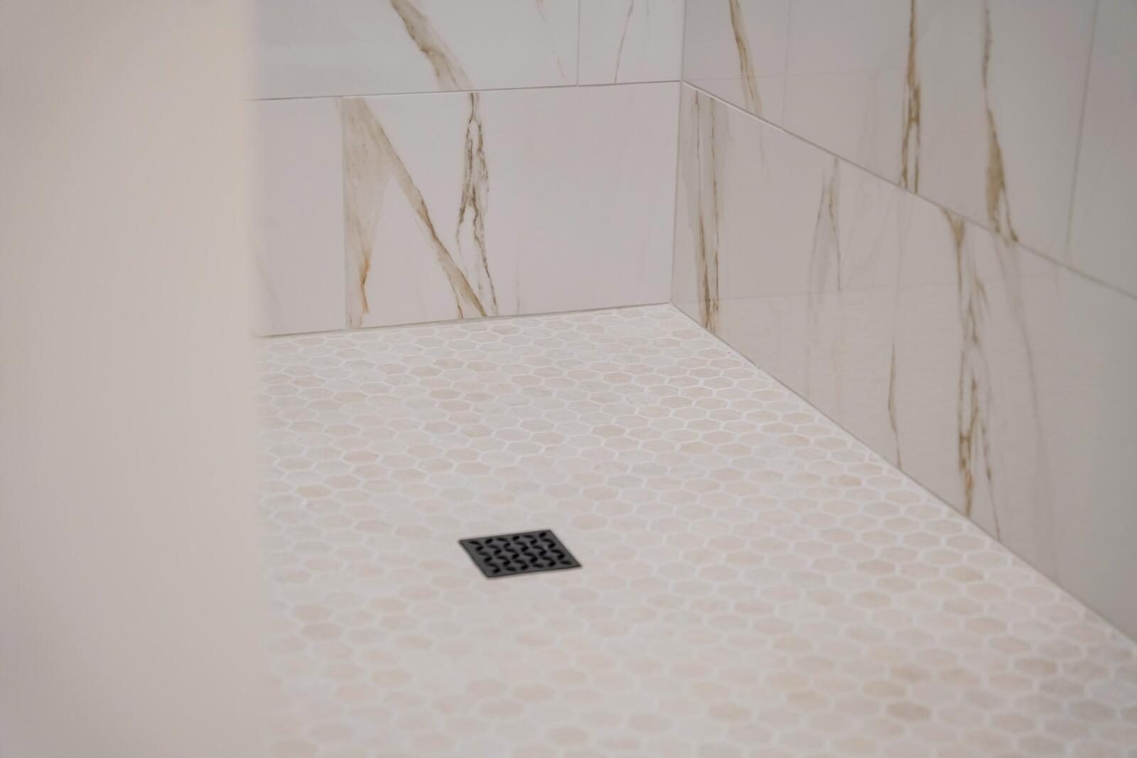 Marble-tiled walk-in shower with hexagon mosaic floor and matte-black drain — custom bathroom detail by KB Builders, Mifflintown, PA