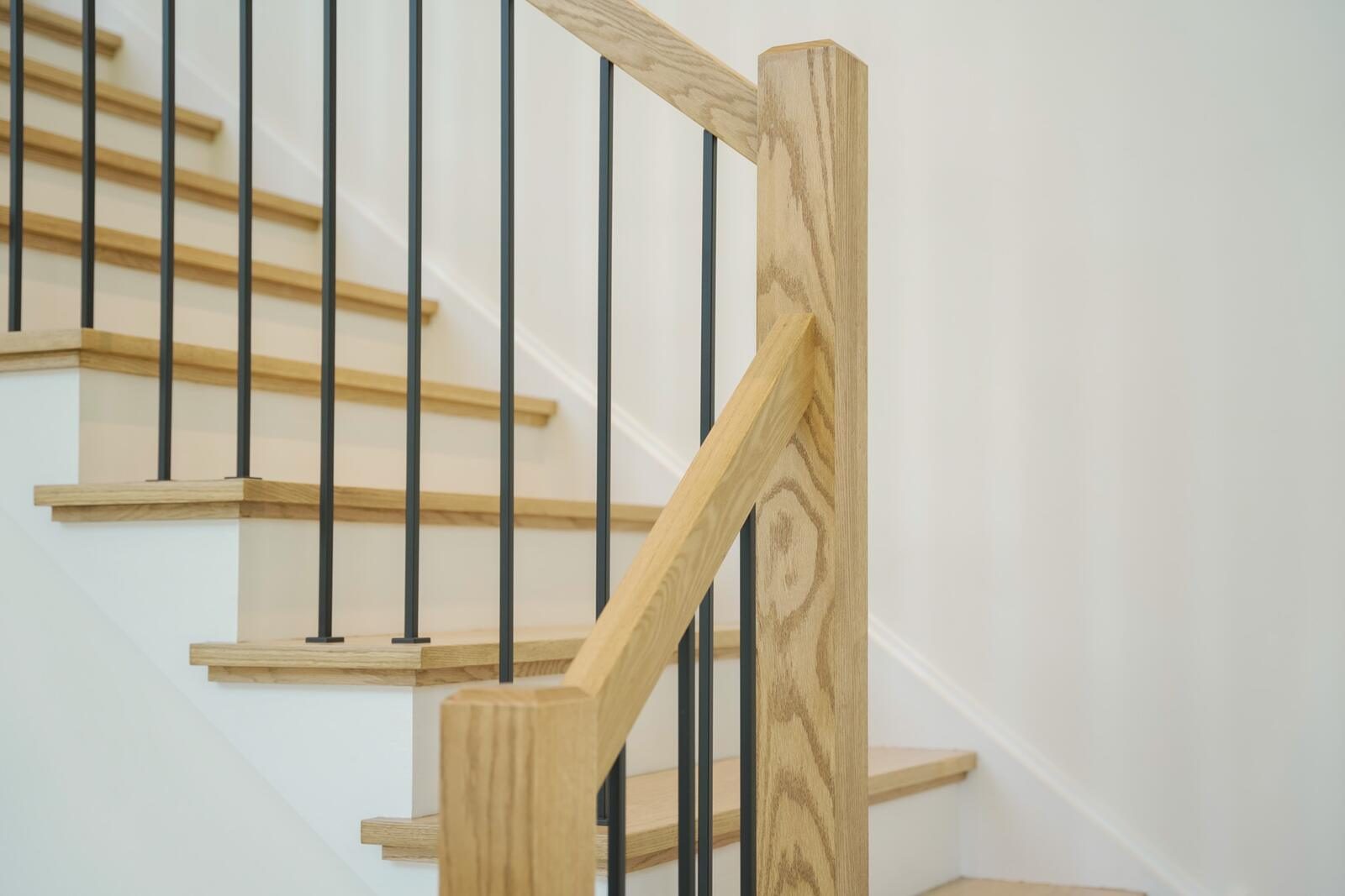 Open-riser staircase detail with red-oak treads, oak newel post, and matte-black iron balusters — KB Builders custom home, Mifflintown, PA