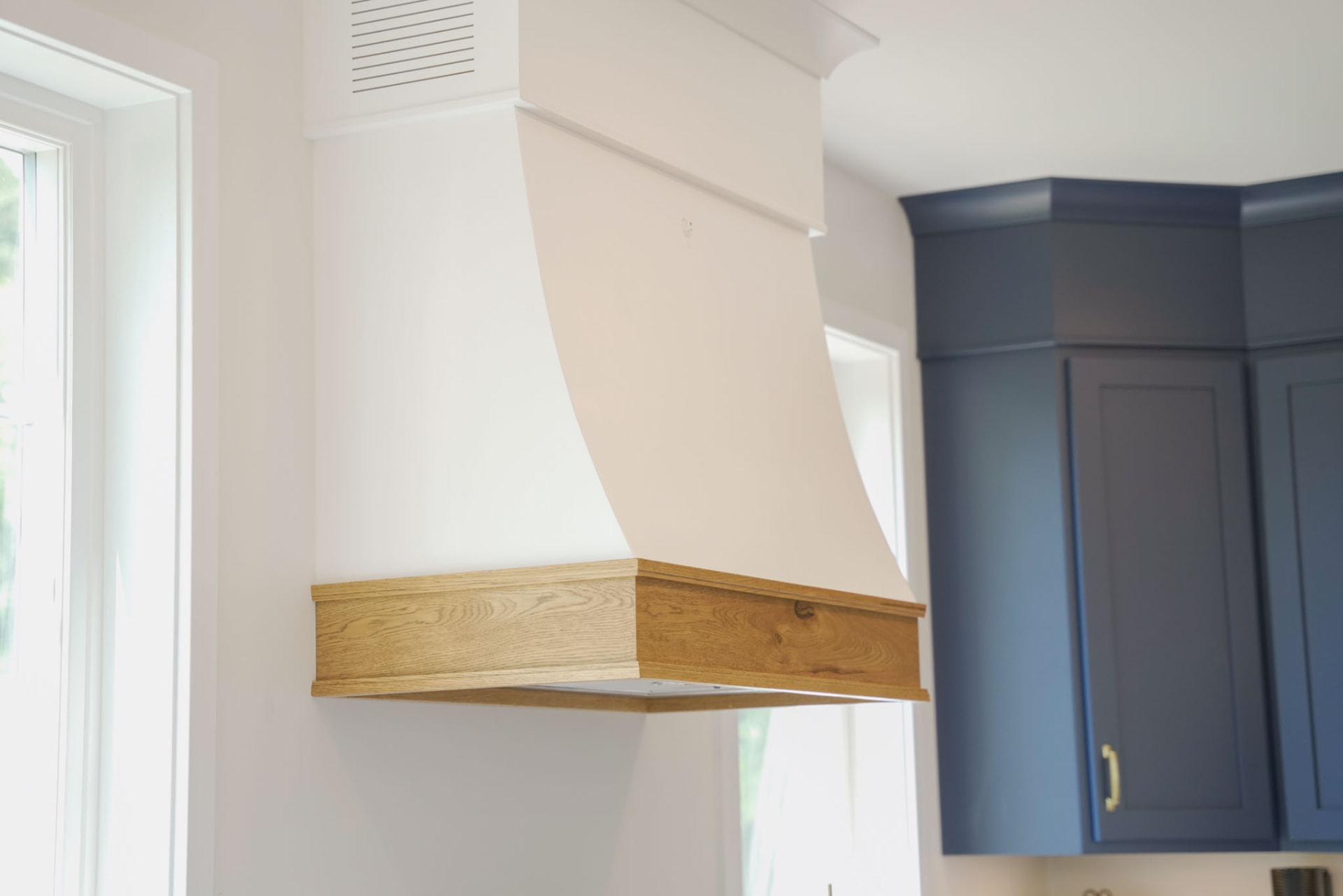 Byler Residence — custom range hood with white oak trim beside navy shaker cabinets — KB Builders, Central Pennsylvania