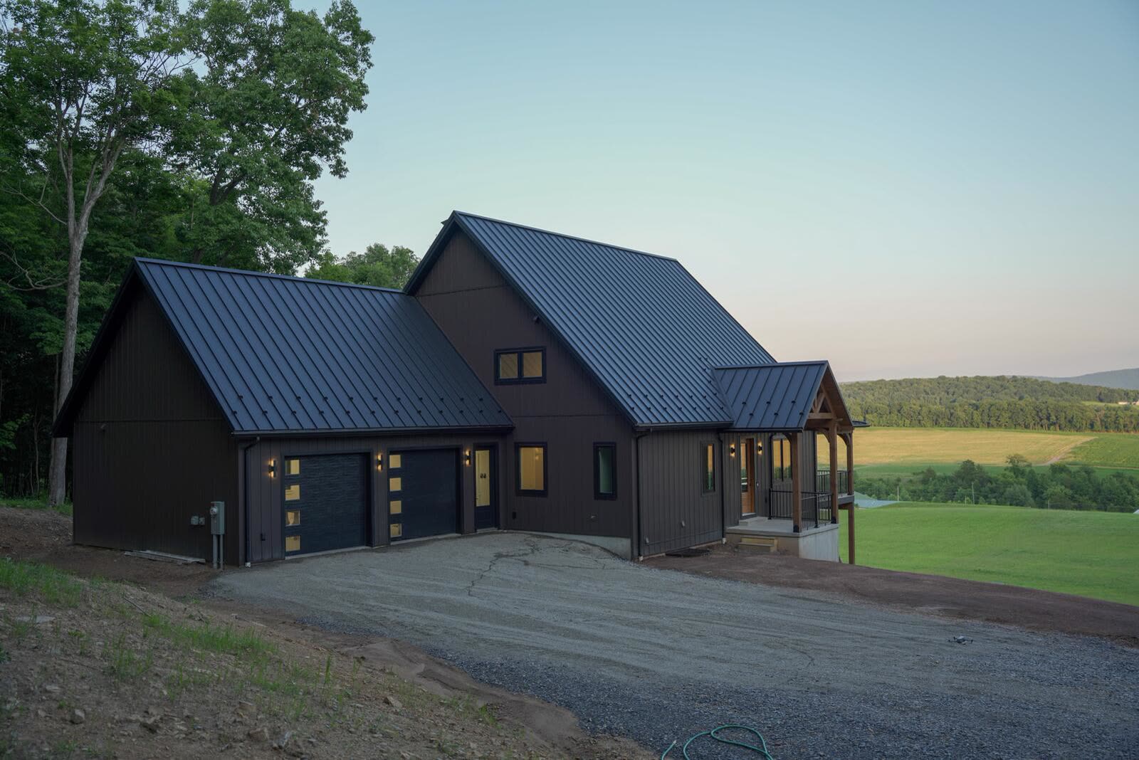 Custom home exterior with dark siding, standing-seam metal roof, and two-car garage overlooking farmland — KB Builders, Mifflintown, PA