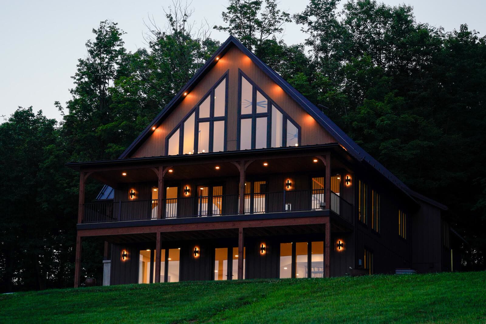 Shetler Residence front elevation at dusk with glowing gable windows and timber-frame porches — custom home by KB Builders in Mifflintown, PA