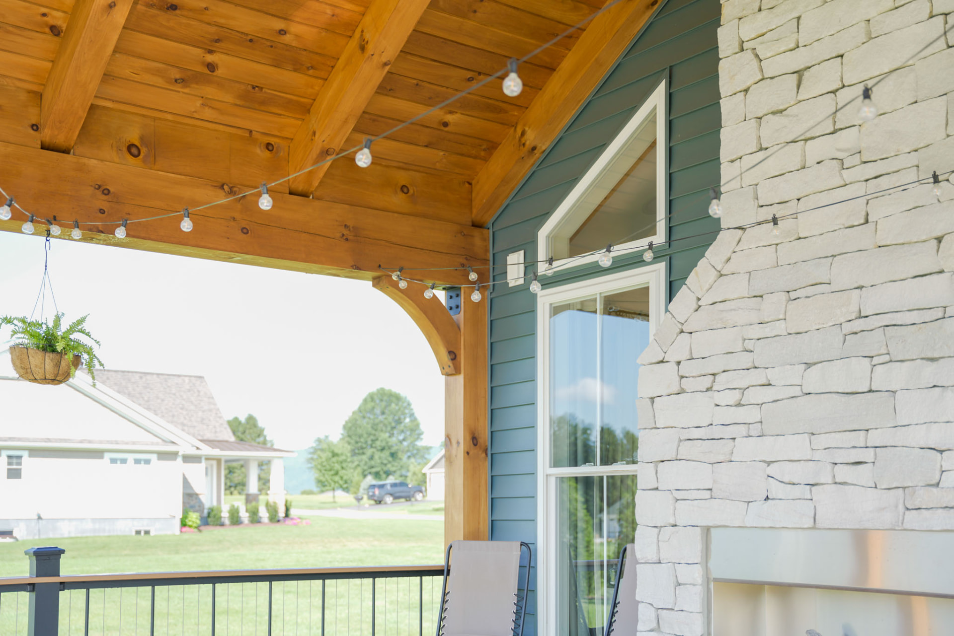 Yoder Residence — covered rear porch with timber trusses, string lights, and stone fireplace — KB Builders, Central Pennsylvania
