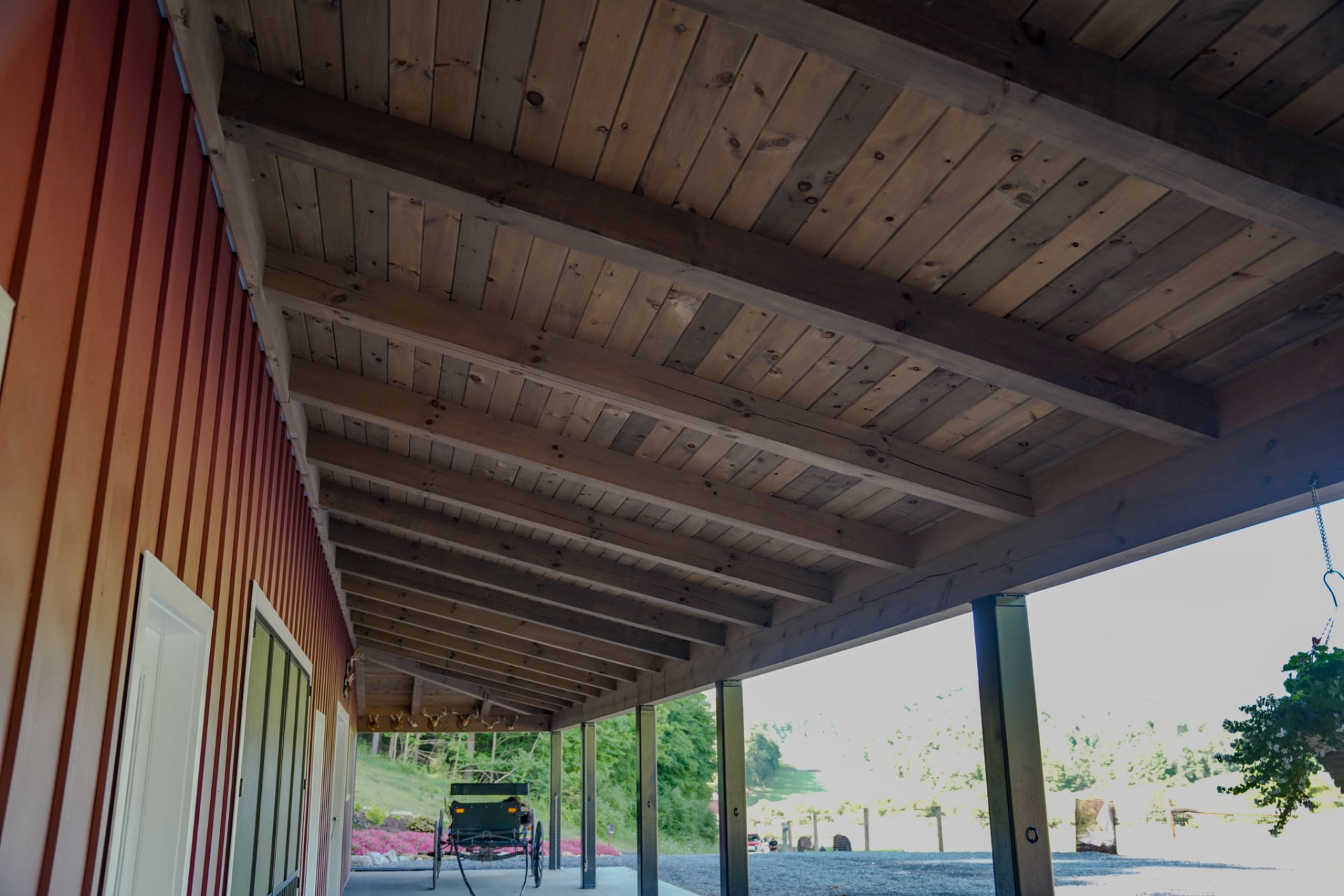 Peachy Residence — exposed timber beams and pine ceiling over the covered porch of a barndominium — KB Builders, McVeytown, PA