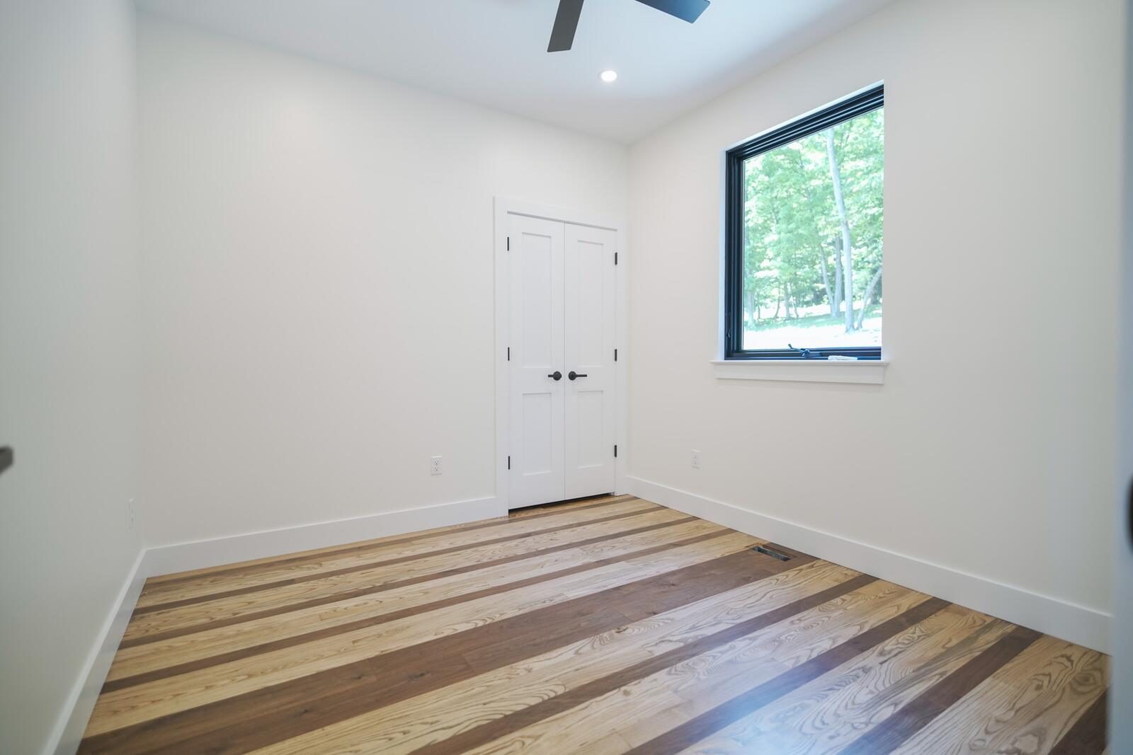 Bedroom with mixed-tone hardwood flooring and oversized picture window framing the woods — custom home by KB Builders, Mifflintown, PA