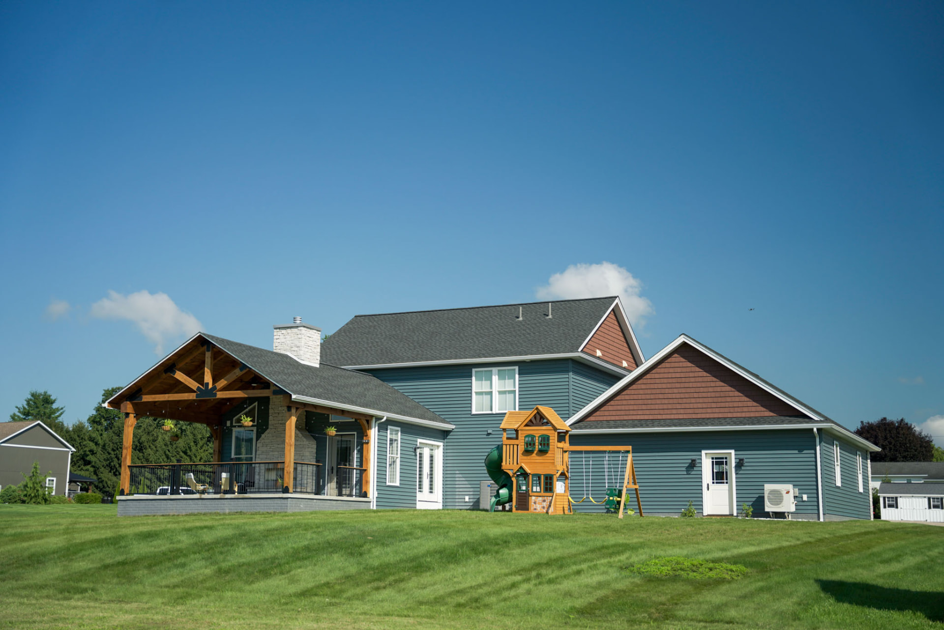 Yoder Residence — rear elevation with timber-framed covered pavilion, stone chimney, and open backyard — KB Builders, Central Pennsylvania