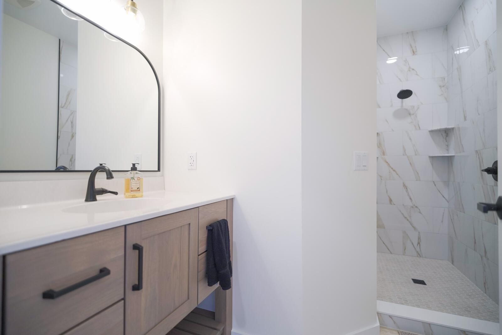 Guest bathroom with floating wood vanity, arched mirror, and marble-tiled walk-in shower — custom home by KB Builders, Mifflintown, PA