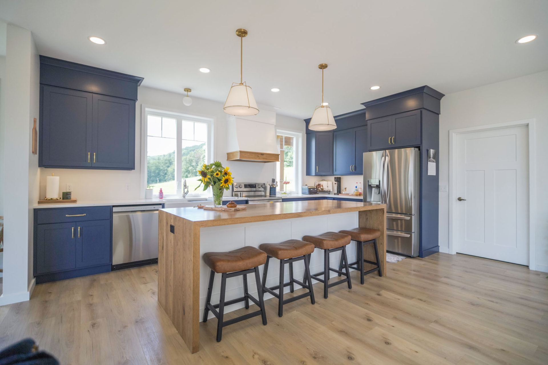 Byler Residence — kitchen with navy shaker cabinets, brass pendants, and oak waterfall island with leather stools — KB Builders, Central Pennsylvania