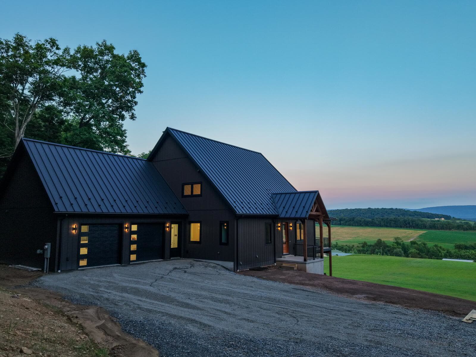 Custom home at dusk with attached garage and timber-frame entry, farmland in the distance — KB Builders, Mifflintown, PA