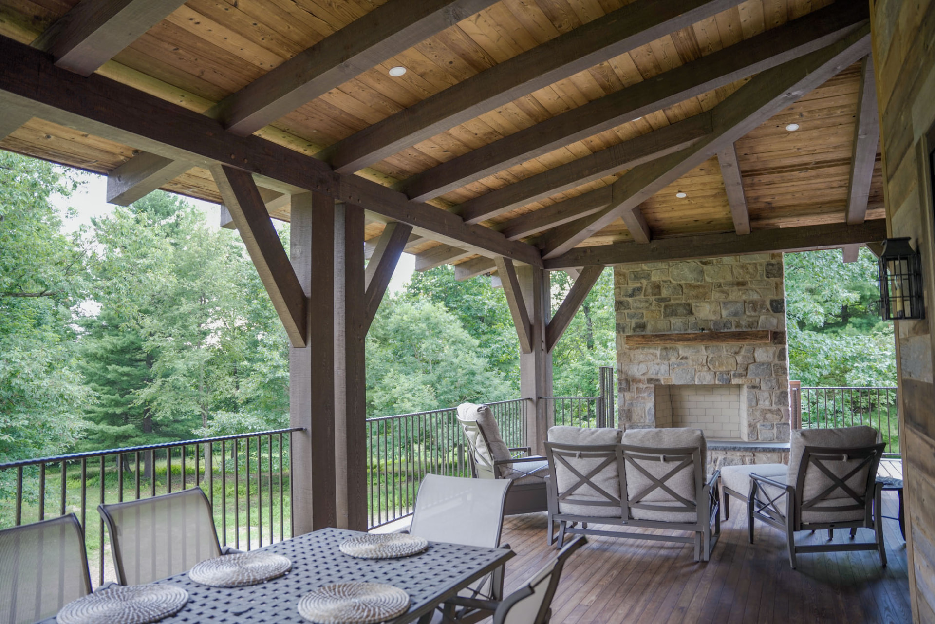 Wright Residence — covered rear deck with stone fireplace, timber rafters, and dining area overlooking the woods — KB Builders, Central Pennsylvania