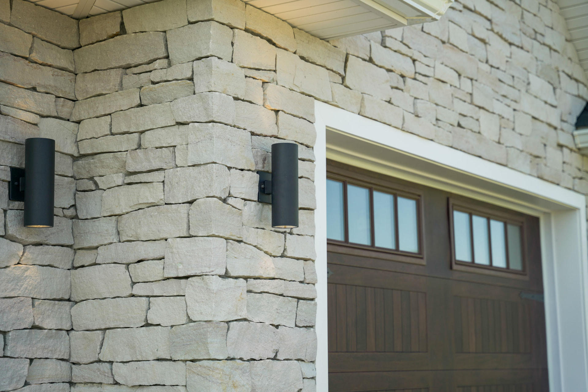 Yoder Residence — hand-laid stone garage wall with black cylinder sconces and carriage-style door — KB Builders, Central Pennsylvania